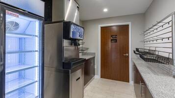 Una cocina con un refrigerador de acero inoxidable, un dispensador de agua y un congelador. Hay una puerta de madera con la leyenda 'Solo personal' y un perchero con ganchos.