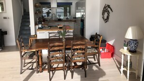 Et spiseområde med et træbord og stole, et køkken i baggrunden, og en trappe, der fører til et andet niveau.