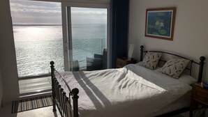 Et soveværelse med et stort vindue der giver udsigt over havet.