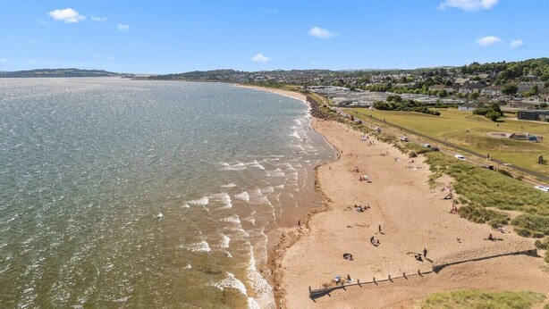 A coastal beach with a sandy shore, a road parallel to the beach, and a residential area in the background. - Panmure Apartment - golf course views (Monifieth)