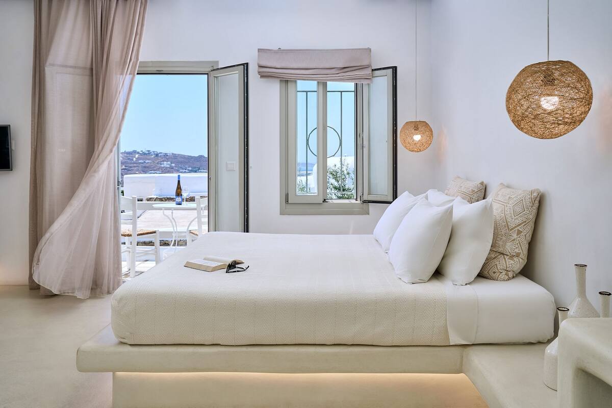 A modern bedroom with a large bed, a view of the city, and a balcony.