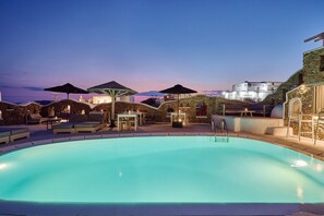 A swimming pool with lounge chairs and umbrellas, surrounded by stone walls and a view of the mountains.
