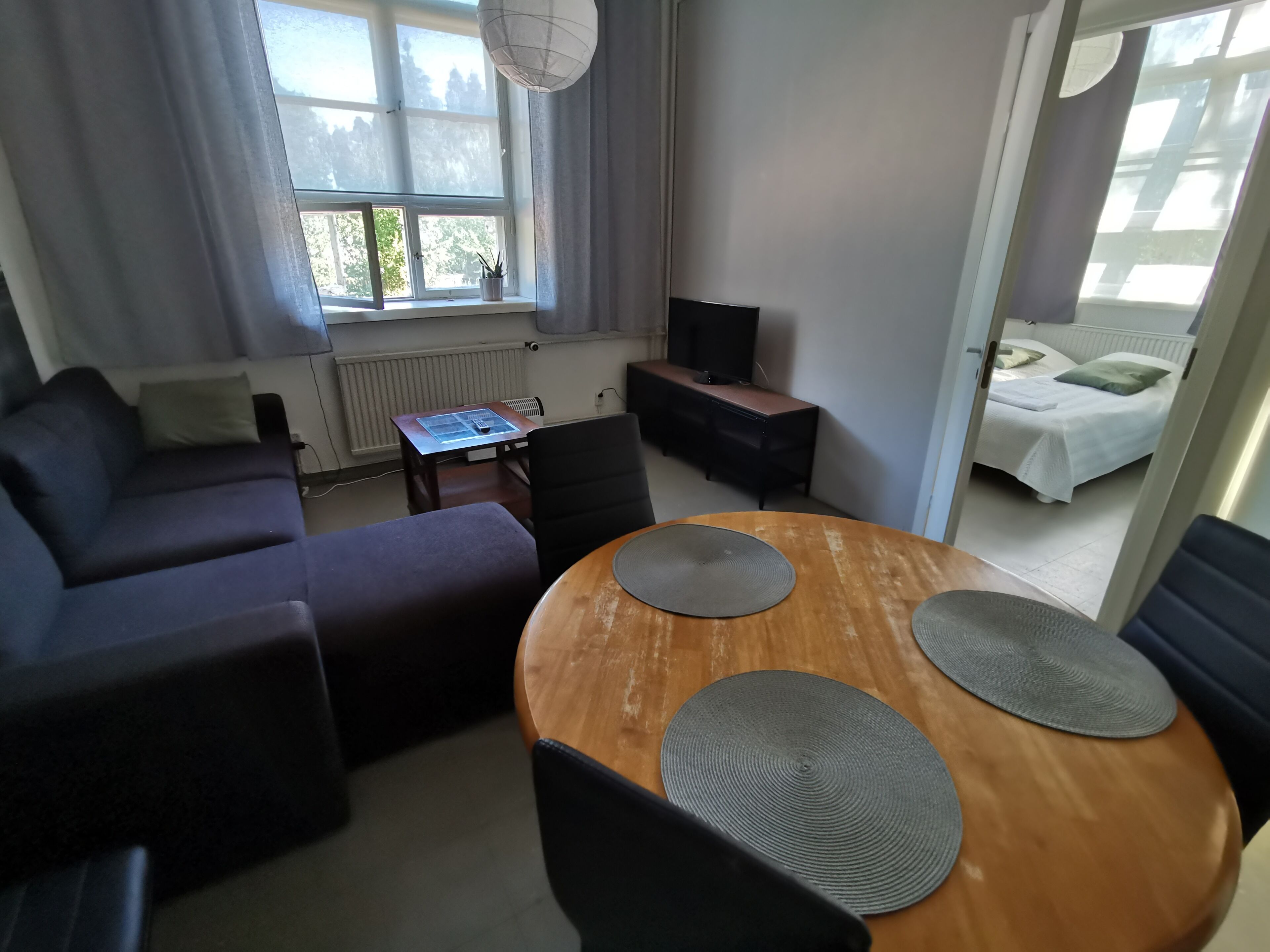 Ein modernes Wohnzimmer mit einer Couch, einem Holzespeisetisch mit Stühlen, einem Fernseher und einem Fenster mit Vorhängen.