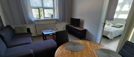 Ein modernes Wohnzimmer mit einer Couch, einem Holzespeisetisch mit Stühlen, einem Fernseher und einem Fenster mit Vorhängen.