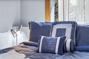 A bedroom with a bed, pillows, and a window with blinds.