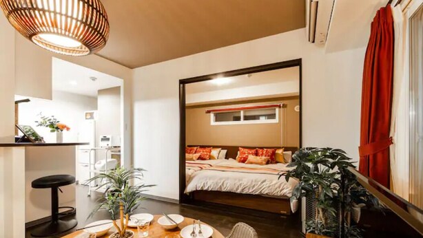 Una habitación de hotel compacta con cama, zona de comedor con mesa y sillas, y kitchenette.