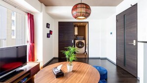 Una sala de estar moderna con televisor, una mesa redonda de madera, una planta en maceta y una lámpara colgante original.