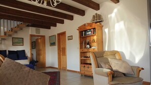 A cozy living room with a wooden staircase, a bookshelf, and a comfortable armchair. - HAuszeit Kapitänshaus Friedrichsschleuse - Temporary home (Wittmund)