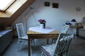 A dining area with a wooden table, white chairs, a vase with flowers, a radio, and a lamp. - HAuszeit Kapitänshaus Friedrichsschleuse - Temporary home (Wittmund)