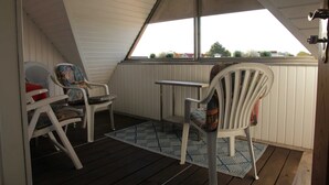 A covered patio with two white chairs, one with a colorful cushion, and a small table. - HAuszeit Kapitänshaus Friedrichsschleuse - Temporary home (Wittmund)