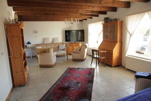 A spacious living room with a wooden ceiling, a television, a sofa, a coffee table, and a patterned rug. - HAuszeit Kapitänshaus Friedrichsschleuse - Temporary home (Wittmund)
