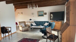 A living room with a blue sofa, a wooden cabinet, a television, and a chandelier. - HAuszeit Kapitänshaus Friedrichsschleuse - Temporary home (Wittmund)