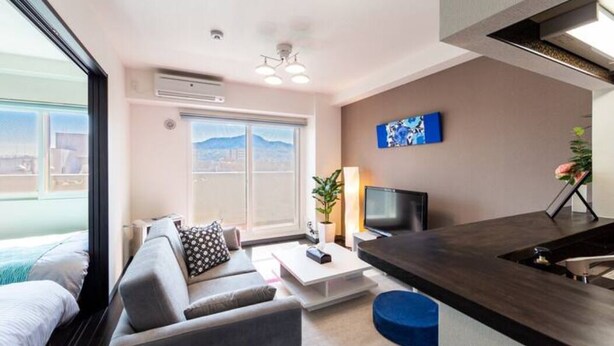 A modern hotel room with a large window, a sofa, a TV, and a small kitchen area. - Edifice (Sapporo)
