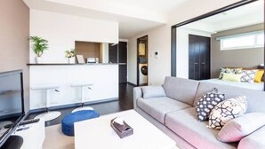A modern living room with a sofa, ottoman, and a flat-screen TV. - Edifice (Sapporo)