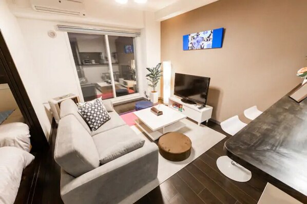 A modern living room with a grey sofa, a coffee table, a TV, and a sliding glass door leading to a balcony.