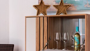 Un meuble en bois sur lequel sont posés une bouteille de vin et des verres, une chaise en osier et, au mur, un tableau représentant des voiliers.