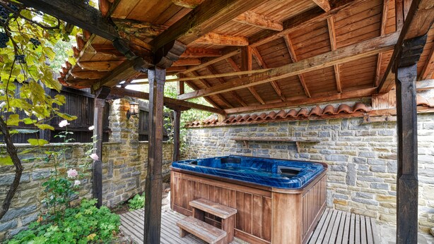 A wooden deck with a hot tub, stone walls, and a pergola structure. - Rent-a-villa with outdoor jacuzzi, BBQ, trampoline and indoor infrared sauna (Medven)