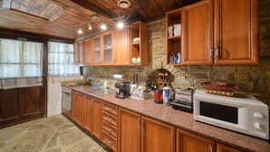 A kitchen with wooden cabinets, a stone wall, and a microwave. - Rent-a-villa with outdoor jacuzzi, BBQ, trampoline and indoor infrared sauna (Medven)