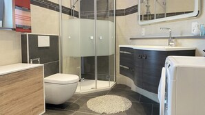 A modern bathroom with a glass-enclosed shower, a toilet, a sink with a mirror, and a built-in washing machine. - Holiday apartment “Hans” (WA324) (Wackersdorf)