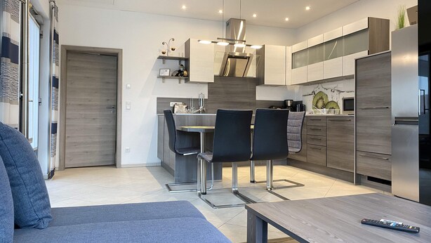 A modern kitchen with a dining area, stainless steel appliances, and a grey sofa. - Holiday apartment “Hans” (WA324) (Wackersdorf)