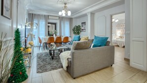 Un salon spacieux avec un canapé gris, un coin repas doté d’une table blanche et un sapin de Noël.
