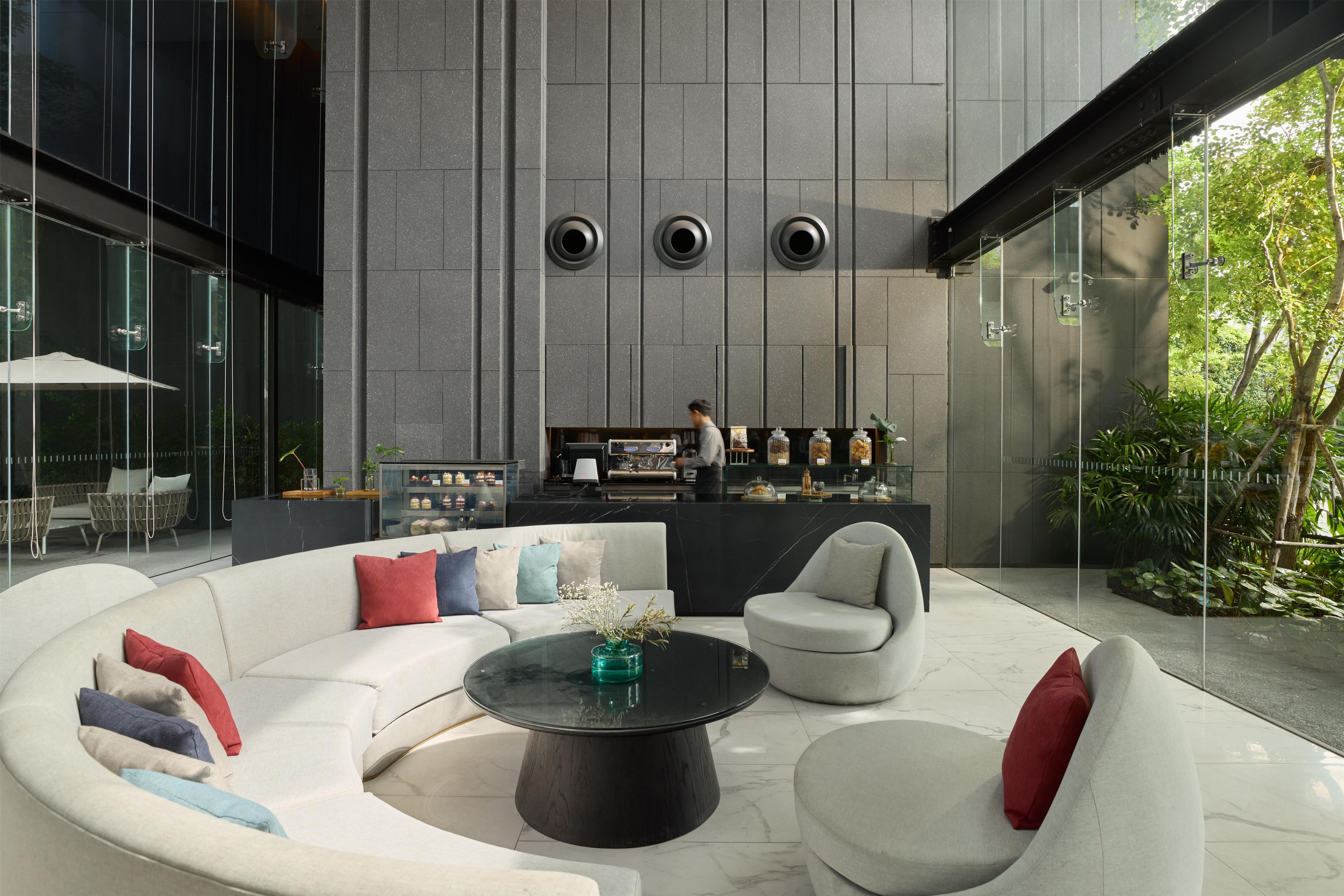 Ein stilvoller Lounge-Bereich mit einer gebogenen weißen Sofagarnitur, einem schwarzen Couchtisch in der Mitte und einer Bar mit einer Person dahinter.