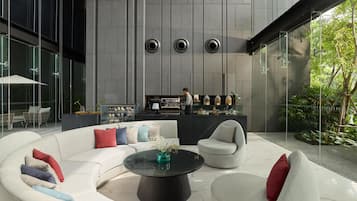 Ein stilvoller Lounge-Bereich mit einer gebogenen weißen Sofagarnitur, einem schwarzen Couchtisch in der Mitte und einer Bar mit einer Person dahinter.
