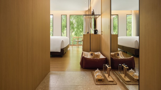 A modern hotel room with two beds, a wooden floor, a large window, and a cozy seating area. - NH Hua Hin (Hua Hin)