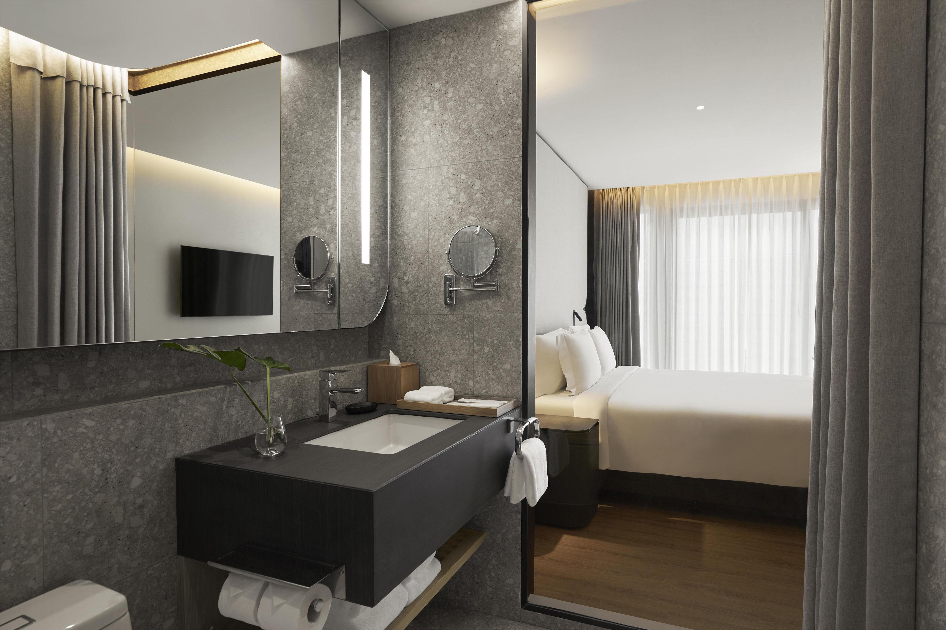 A modern hotel bathroom with a large mirror, a sink, and a toilet.