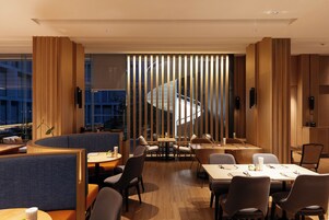 A modern dining area with high tables, comfortable seating, and a view of a spiral staircase.