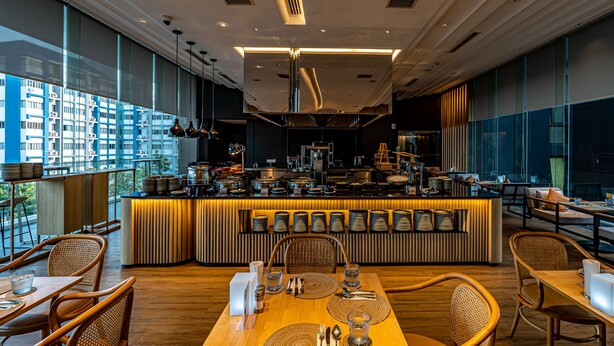 Um restaurante moderno com um bar central, mesas e cadeiras de madeira.