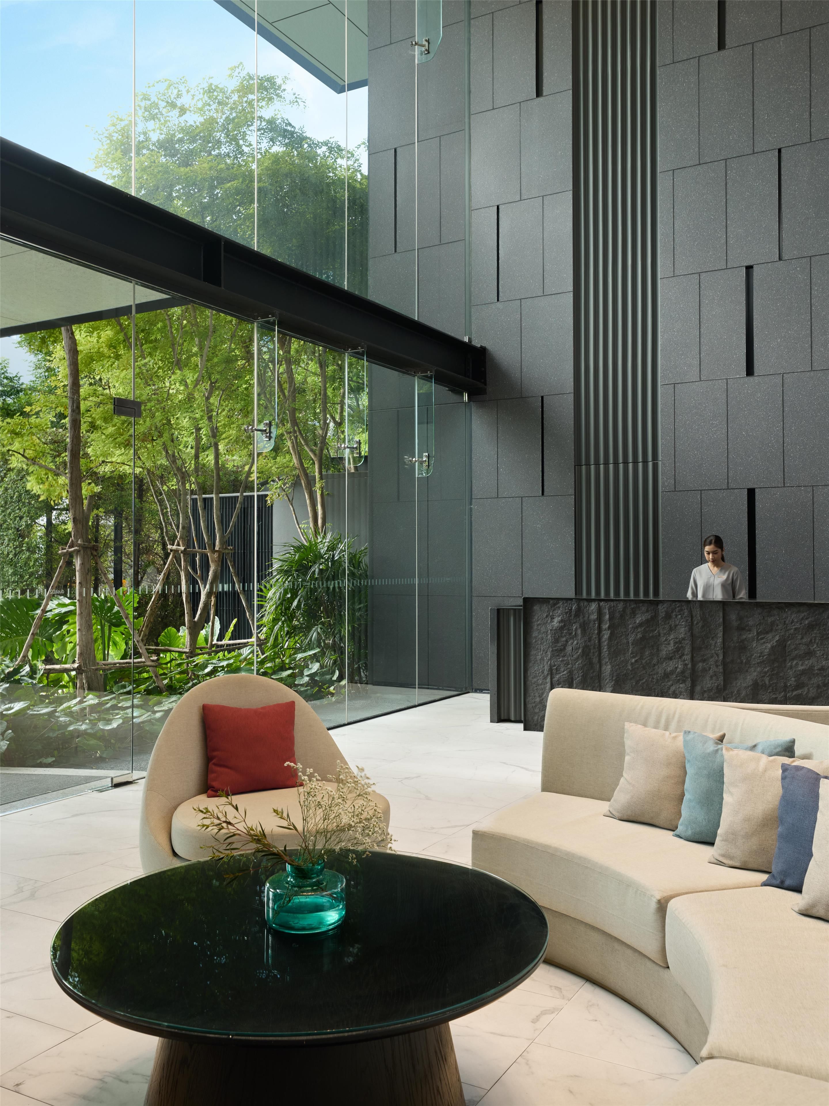 A modern interior with a glass wall, a sofa, a coffee table, and a person in the background.