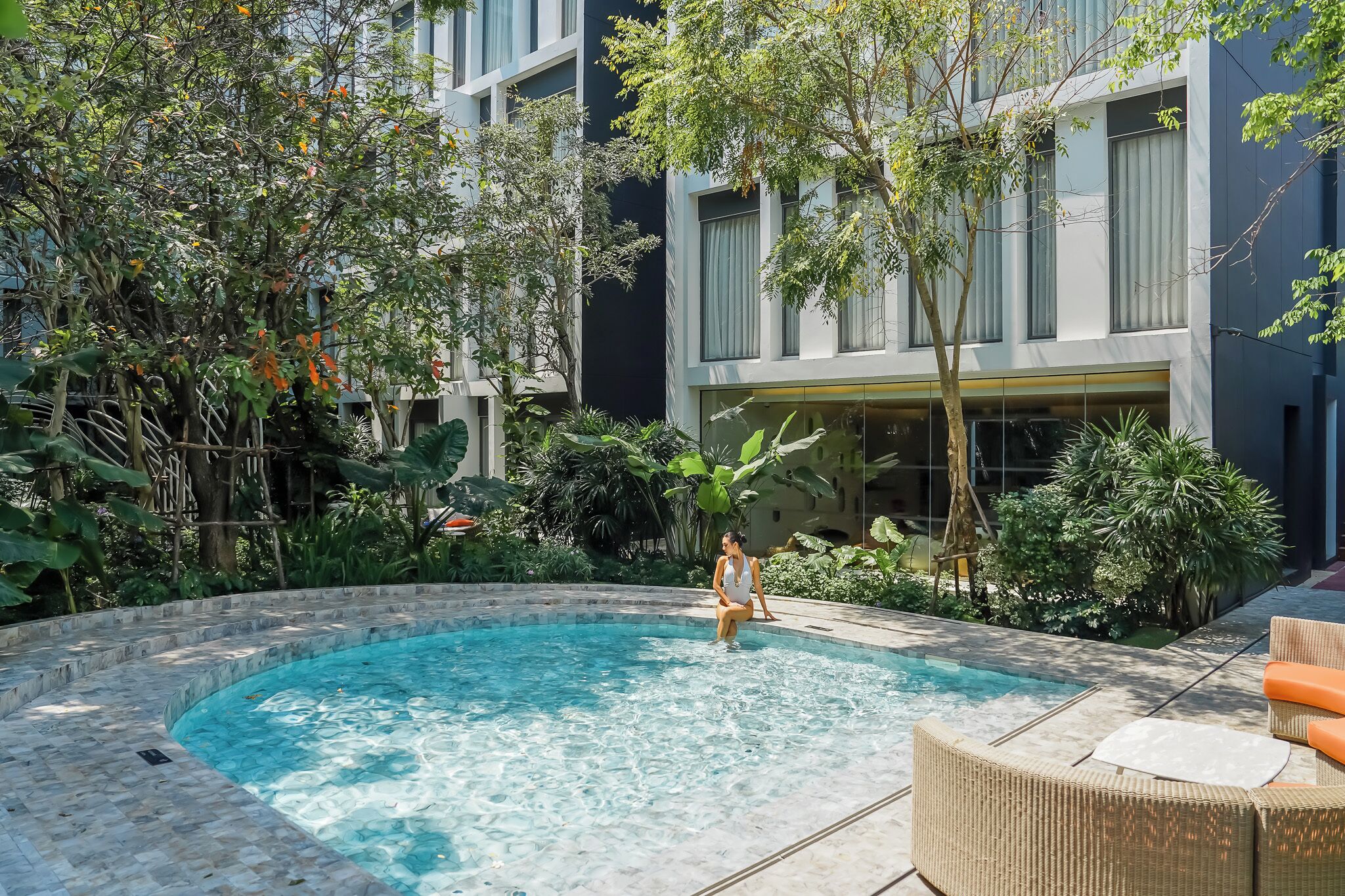 A swimming pool with a tiled edge, surrounded by lush greenery and a building with large windows.