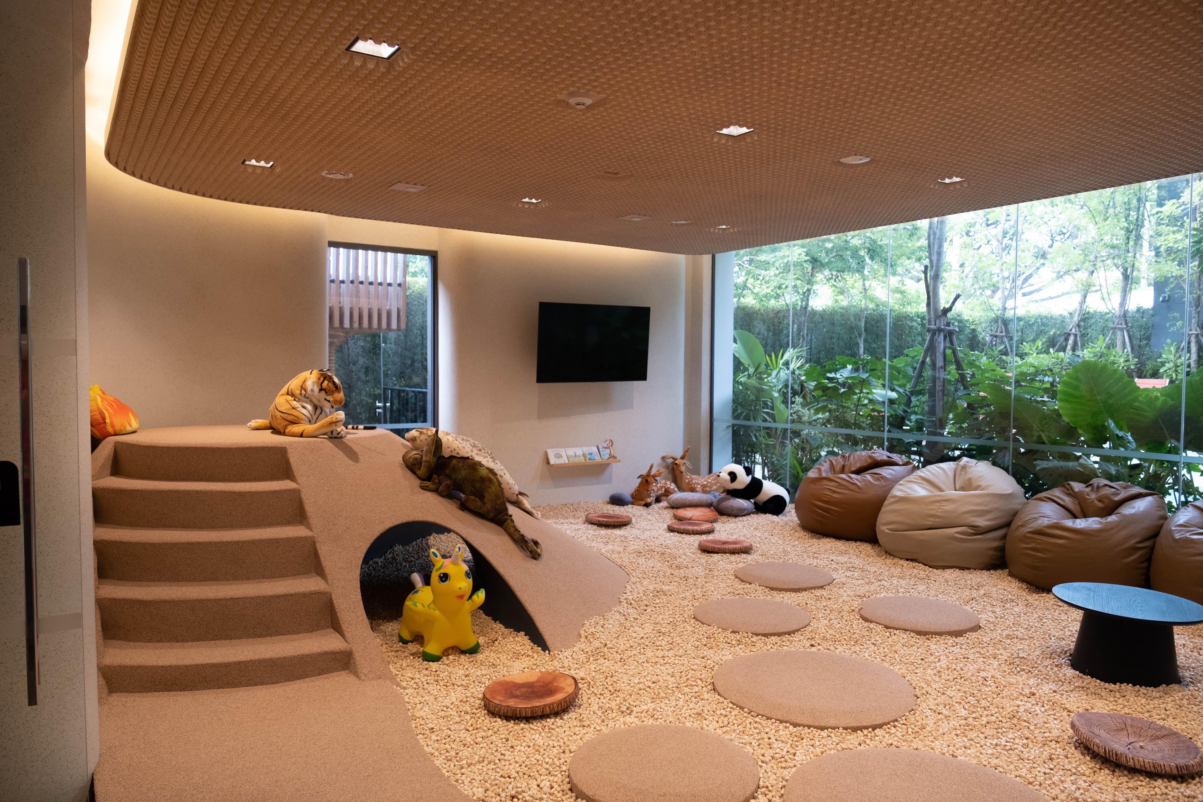 A modern interior with a staircase, plush seating, a television, and a view of greenery outside.
