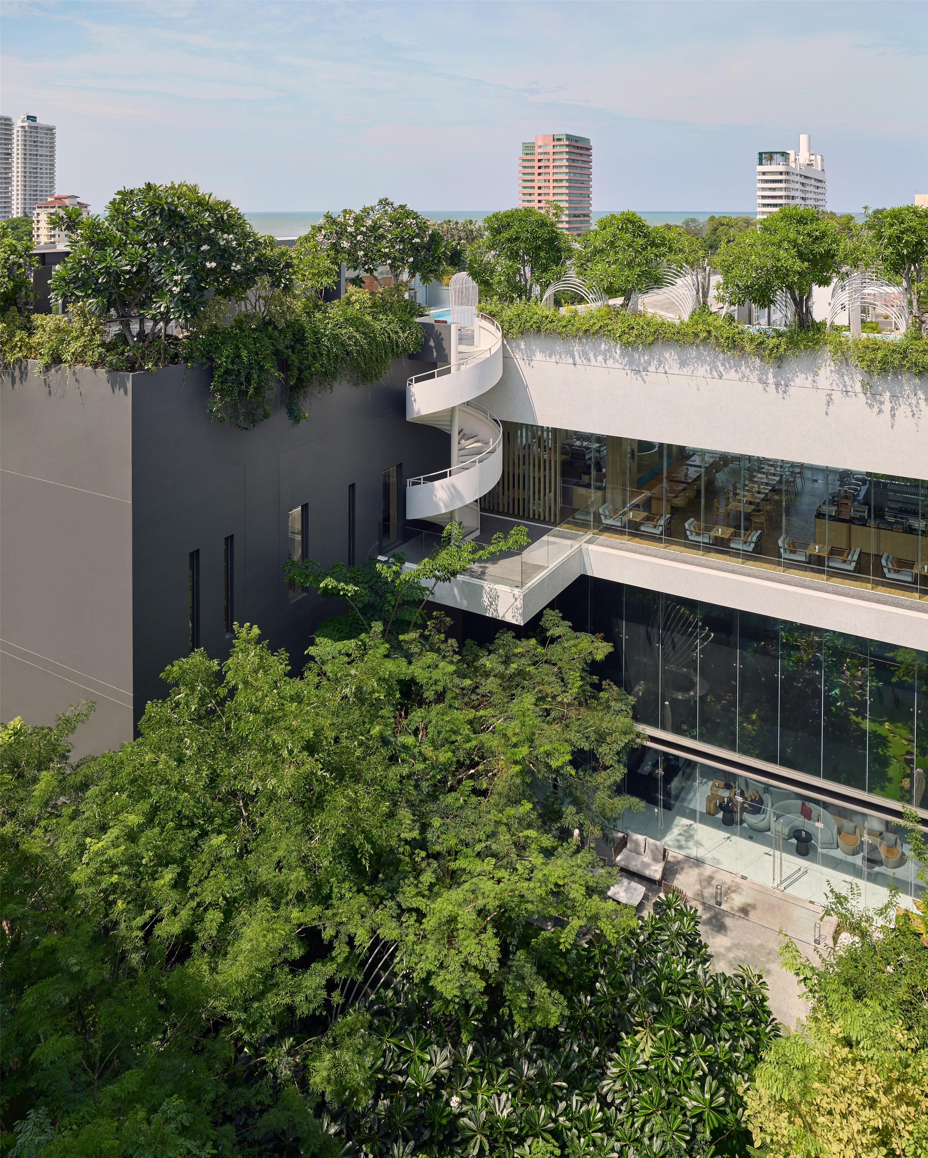A modern building with a rooftop garden, glass walls, and outdoor seating.