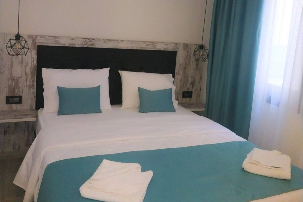 A neatly made bed with a teal bedspread and white pillows, a wooden headboard, and a nightstand with a lamp.