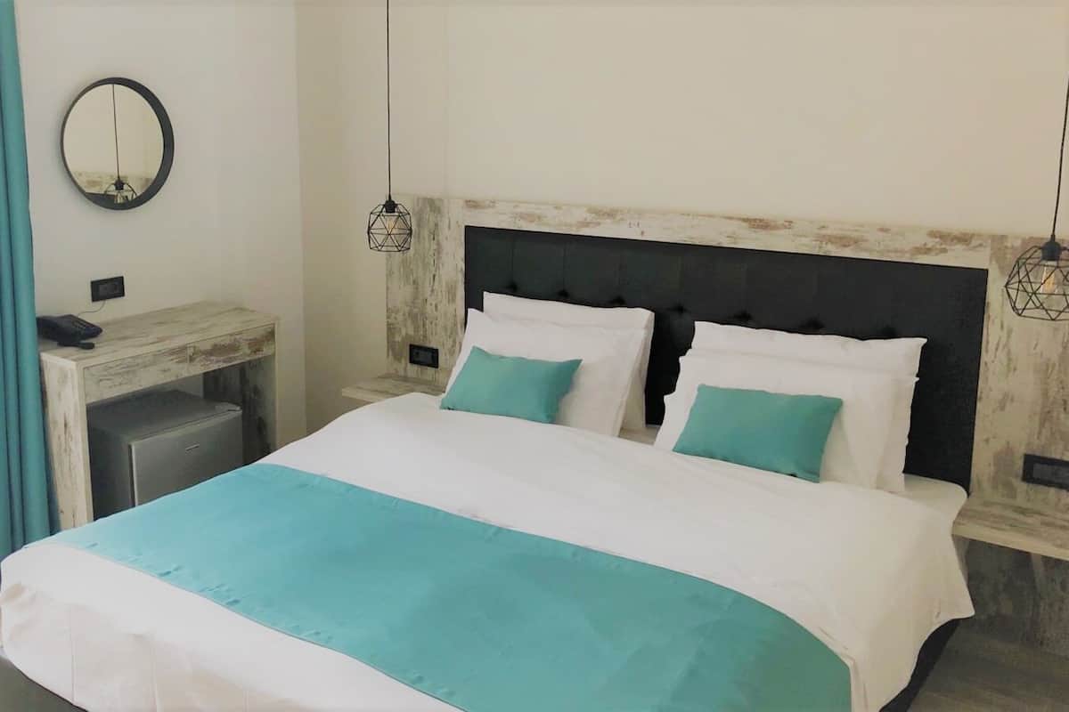 A bedroom with a bed, bedside tables, a desk, a mirror, and a hanging light fixture.