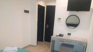 Ein Hotelzimmer mit Bett, Schreibtisch mit Telefon, Spiegel und kleinen Mülleimer.