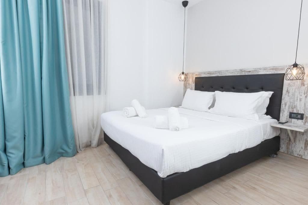 Una cama bien hecha con ropa blanca y toallas, un cabecero oscuro y una mesita de noche con una lámpara.