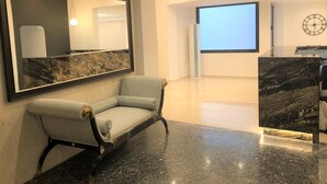 Eine moderne Lobby mit einer мраморной Empfangstheke, einem hellen Sessel und einem großen Spiegel an der Wand.