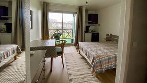Habitación de hotel con dos camas, una mesa de comedor, una silla, una pequeña kitchenette y vista al exterior.