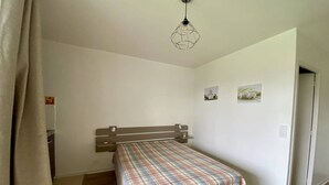 Un dormitorio con cama, cabecera de madera, mesita de noche pequeña y lámpara colgante.