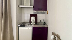 Una cocina compacta con lavavajillas Bosch, una cafetera y un armario morado sobre el lavabo.