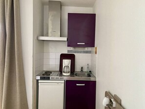 Uma cozinha compacta com máquina de lavar louça Bosch, cafeteira e armário roxo sobre a pia.