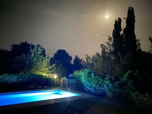 A swimming pool at night with surrounding trees and a distant building. - Villa Yason Private Heated Pool Within Easy Reach Of Beaches, Tavernas & Shops. (Ionian Islands)