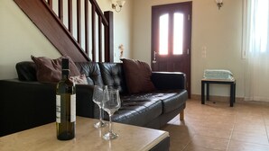A living room with a dark leather sofa, a small table with a wine bottle and glasses, a staircase, and a door with a window. - Villa Yason Private Heated Pool Within Easy Reach Of Beaches, Tavernas & Shops. (Ionian Islands)