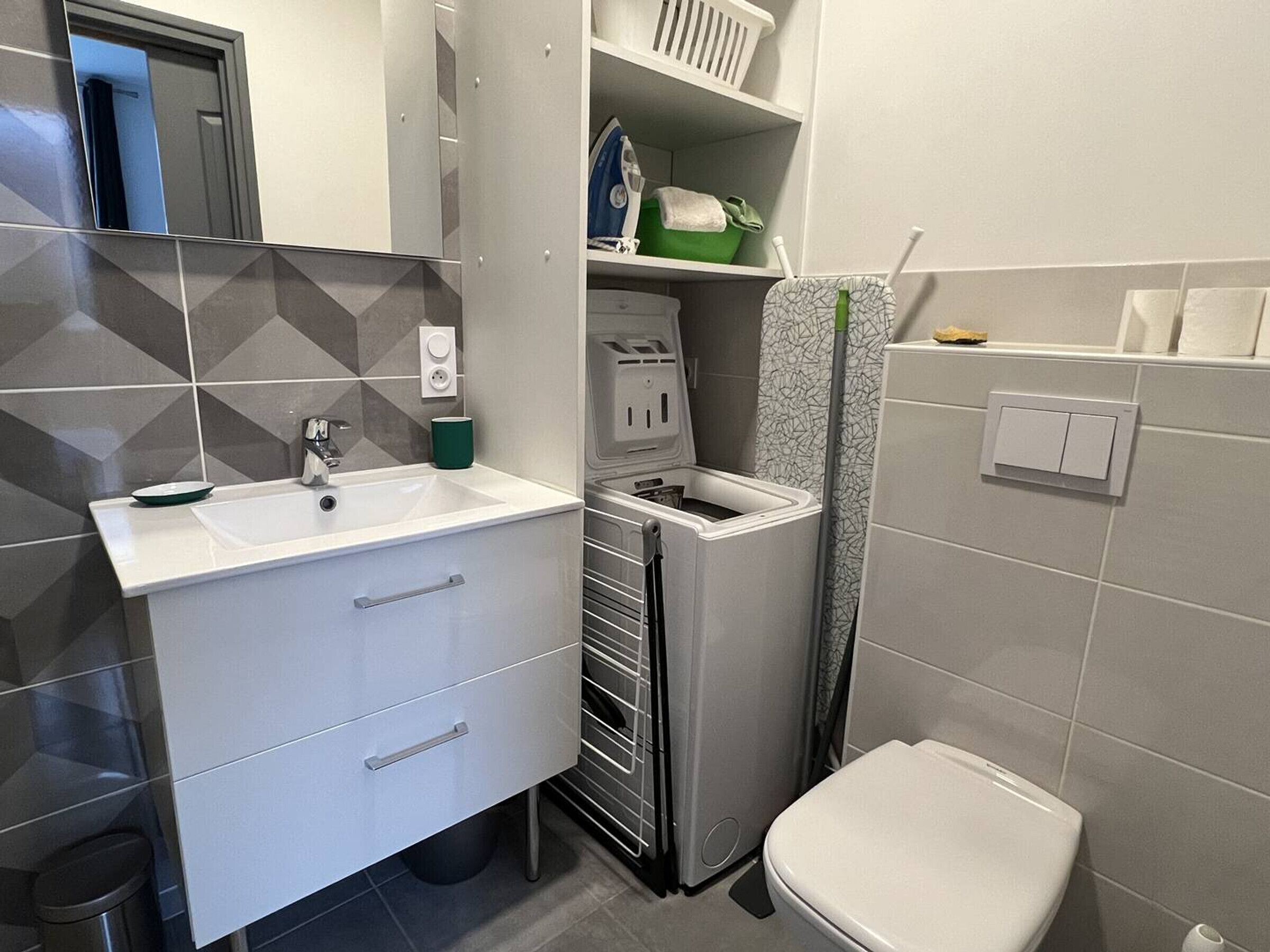 A modern bathroom with a white sink, a toilet, and a compact washing machine.