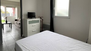 Un dormitorio con cama, televisor en una cómoda, ventana y puerta que da a otra habitación.