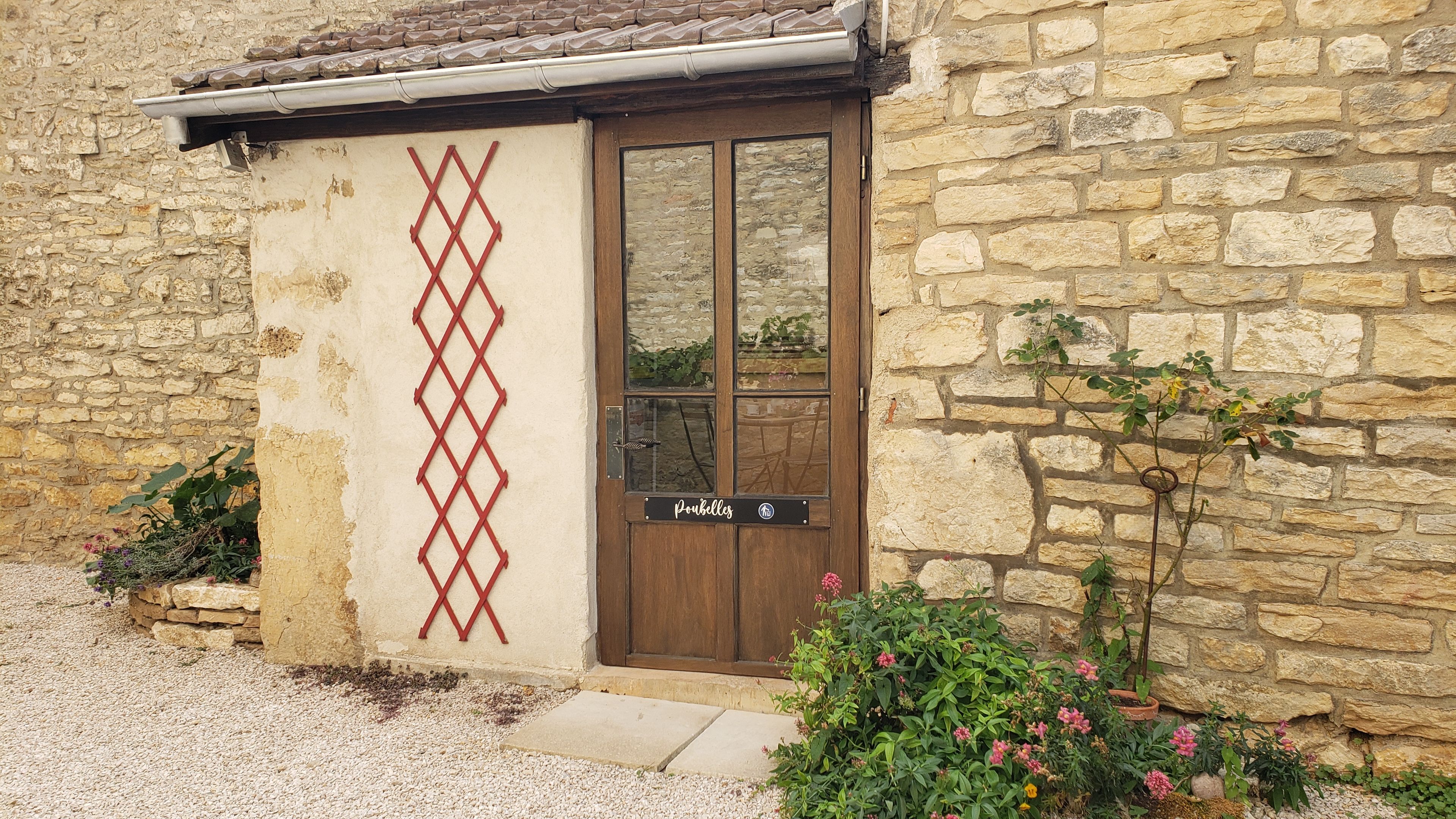 A stone building with a wooden door, a red lattice design, and a sign reading 'Pouilles.'