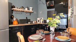 A modern kitchen with a dining table set for two, featuring a coffee maker, toaster, and a vase with flowers. - L'autre Bout de Toit (Meursault)